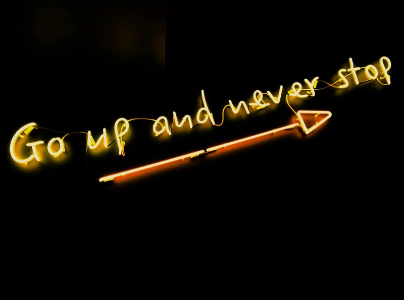 A glowing neon sign that says “Go up and never stop” with an arrow pointing right.