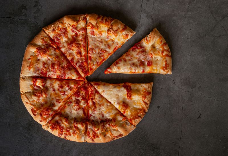 A pizza on a dark surface with one slice pulled away to represent a fraction of the whole.
