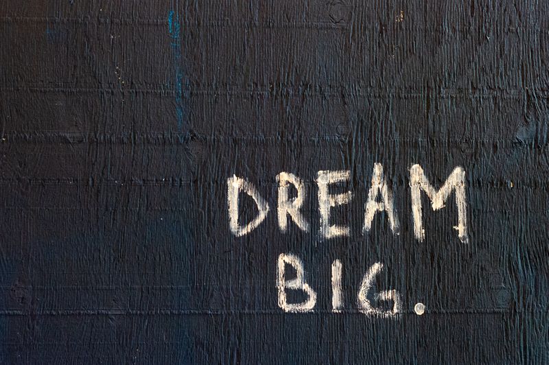 Graffiti on a black wall that reads, 'Dream big'.