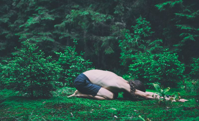 A person in a forest doing the child's pose.
