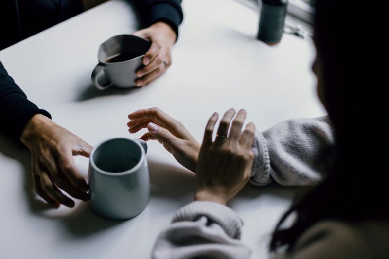 One pair of hands holds a mug while offering another mug to a second pair of hands.