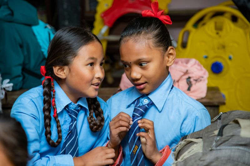 Two school girls in uniforms talking to each other.
