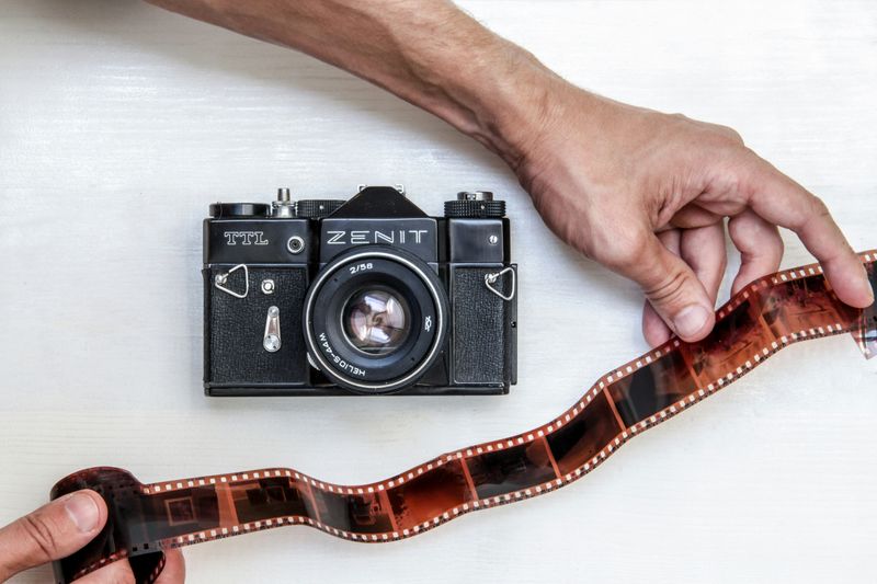 A Zenit film camera on a table with hands unrolling film negatives.