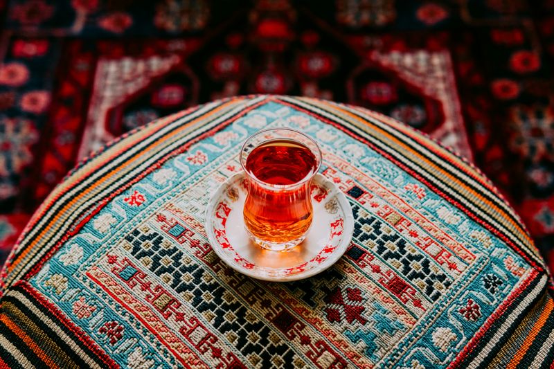 An image of a glass of black tea placed on a Persian carpet