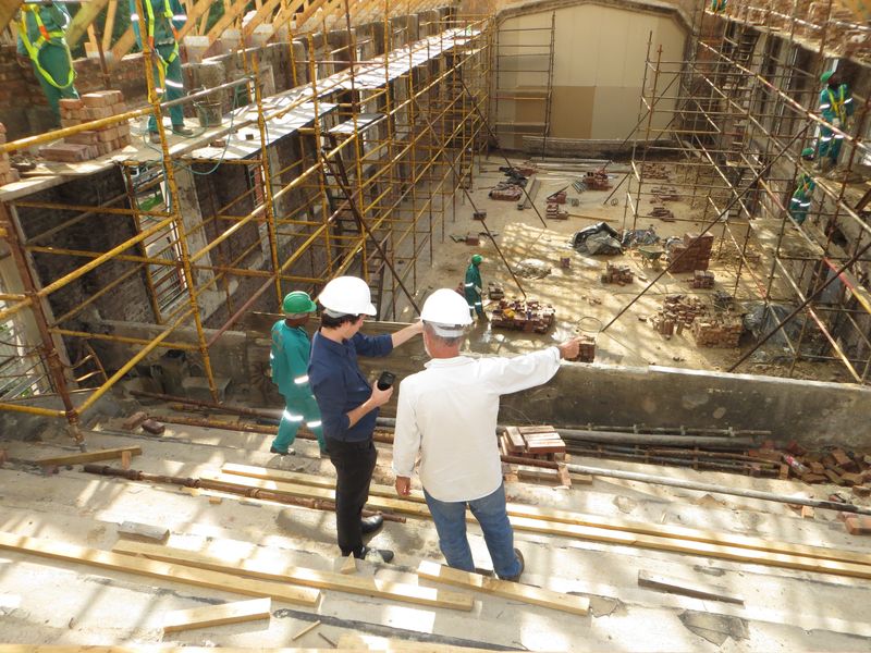 A construction site with two men standing, wearing hard hats and pointing at something in the distance