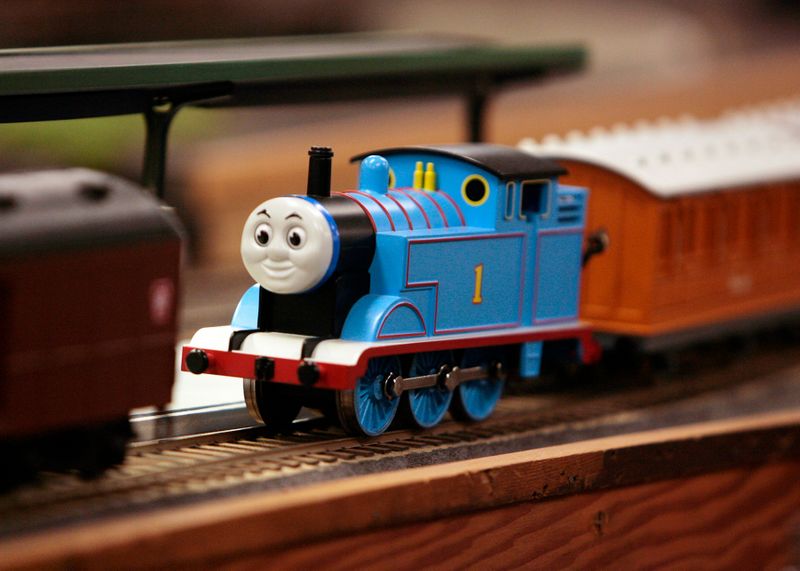 A Thomas the Tank Engine toy on a track with other toy train cars.