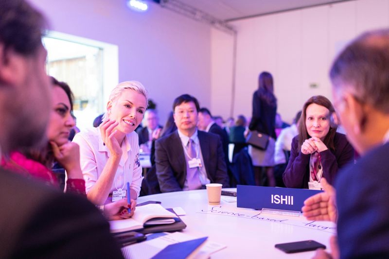 A group of people seated around a table in a conference setting, engaged in a discussion and exchanging ideas.