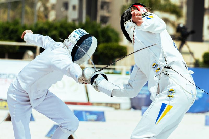 Two fencers compete in an arena.