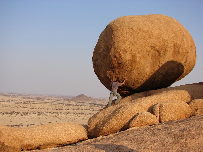 A man standing on a rock while pretending to hold up a boulder.