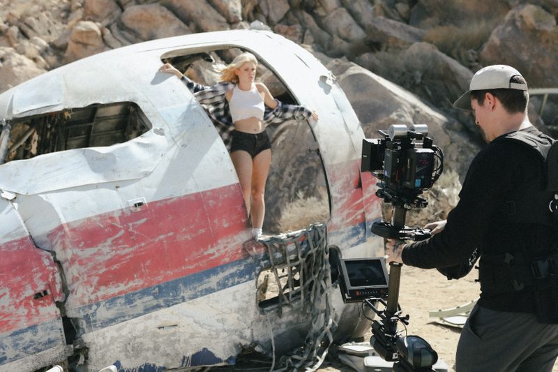 Image of a steadicam operator shooting a scene with a woman posing on a wrecked airplane.