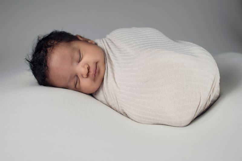 A swaddled baby sleeps with a slight smile. 