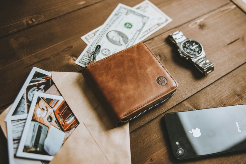 Photo of items that represent money (wallet, phone, expensive watch, money).