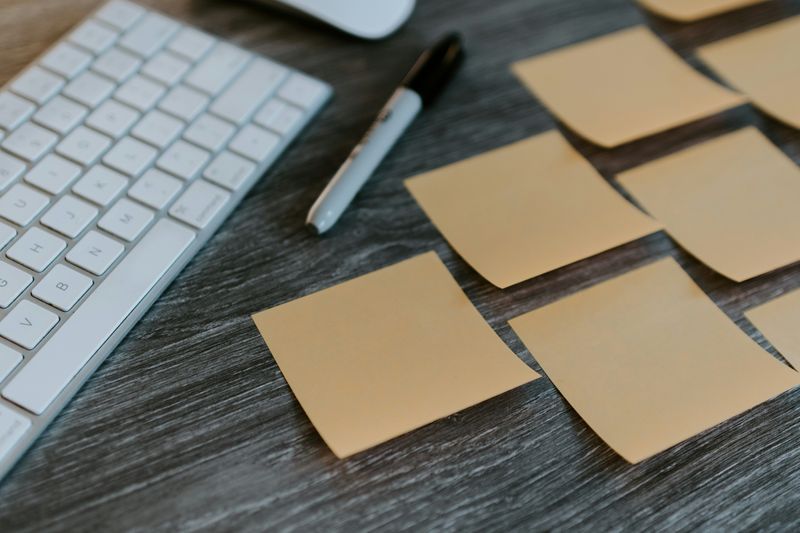 A computer keyboard, a pen, and several sticky notes on a desk.