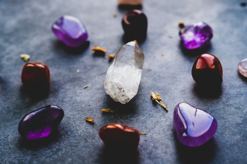 Different gems on a dark background. The shiny gems are dark red, purple, and clear crystals.