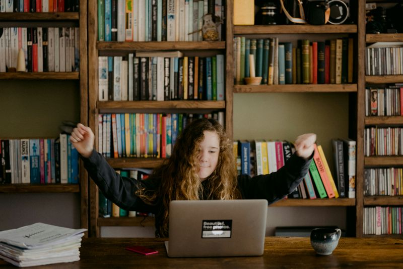 A student at a computer learning. She raises her hands in the air with enthusiasm.