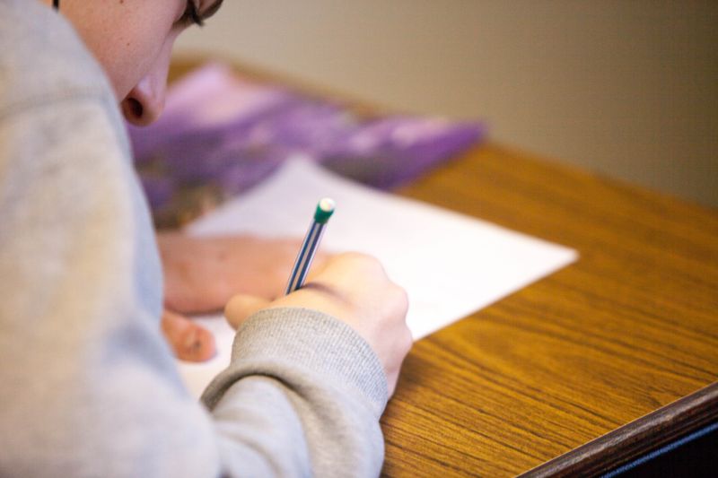 A student sitting at a desk writing with a pencil