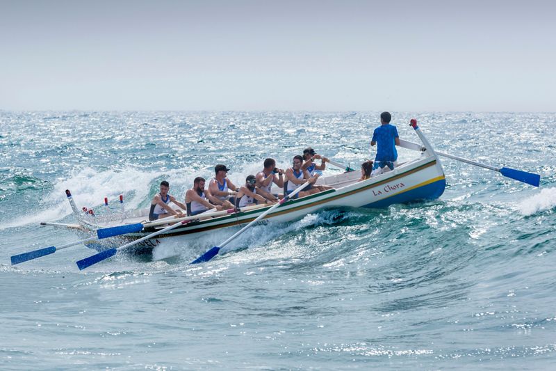 A rowing team with a leader at the front of the boat, using emotional intelligence skills to lead them through rough waves.