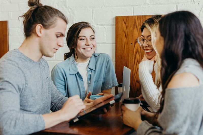 A group of young professionals collaborating and smiling during a casual team meeting with laptops and coffee.