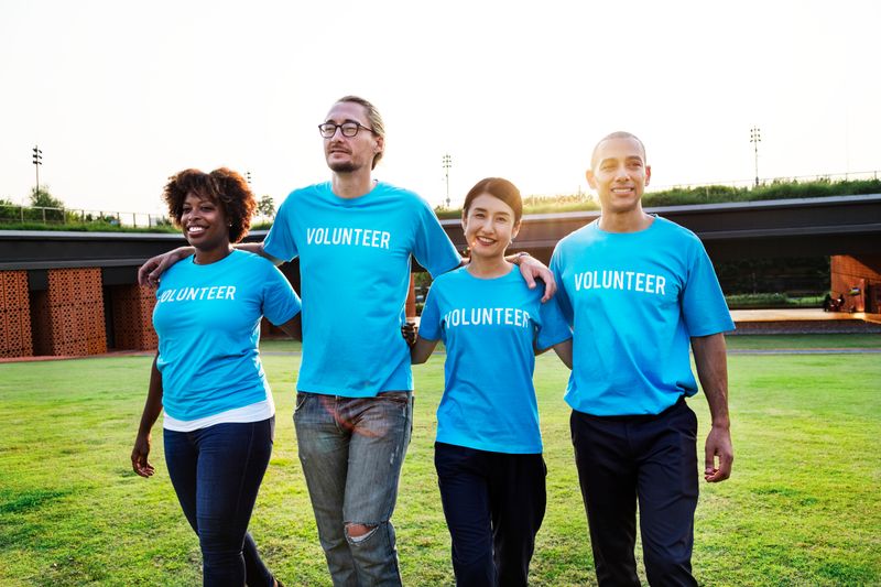 Photo of four volunteers, arms draped over each other's shoulders, wearing blue "Volunteer" t-shirts.