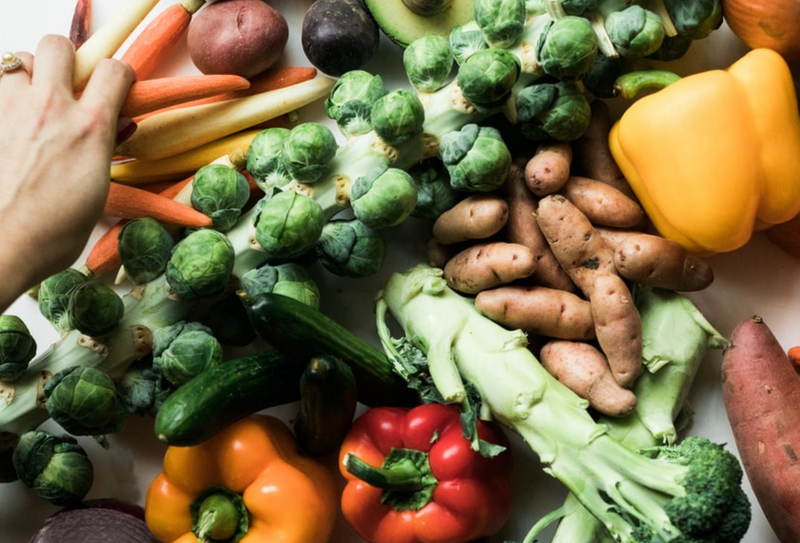 A hand grabbing vegetables that are spread out on a table.