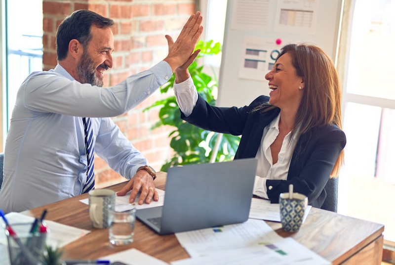 Man and Woman In an office setting giving each other a high-five and smiling. 