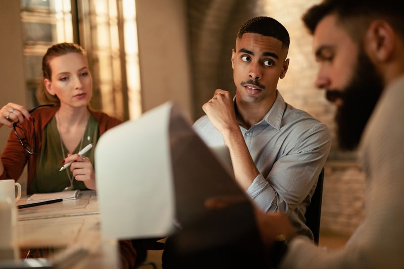 A man in a meeting looks unsure about what his colleague is saying.