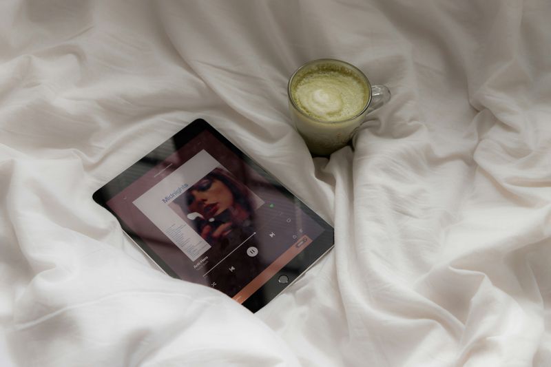 Taylor Swift playing on an iPad lying on a bed beside a cup of macha.