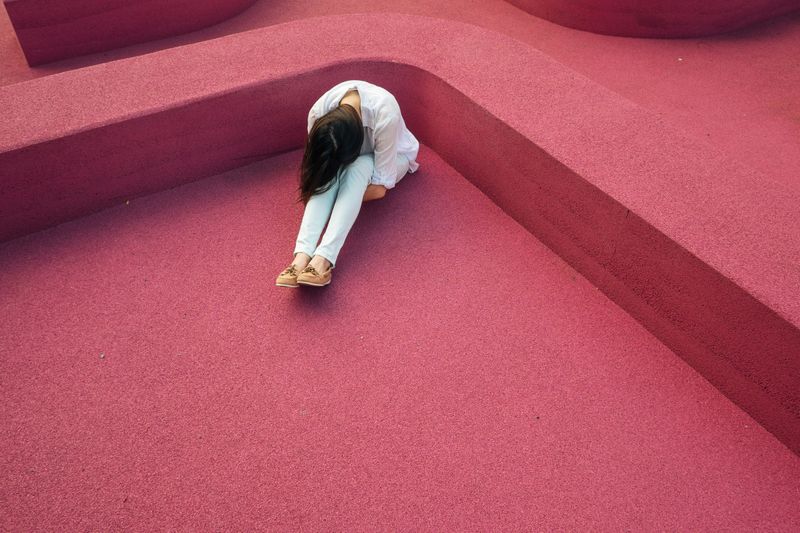 A girl sitting alone by herself. She stretches out her legs and rests her head on her knees.