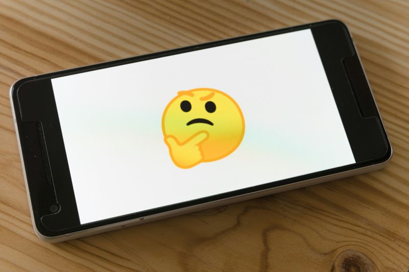A smartphone displaying a thinking face emoji on a wooden surface, symbolizing self-reflection or decision-making.