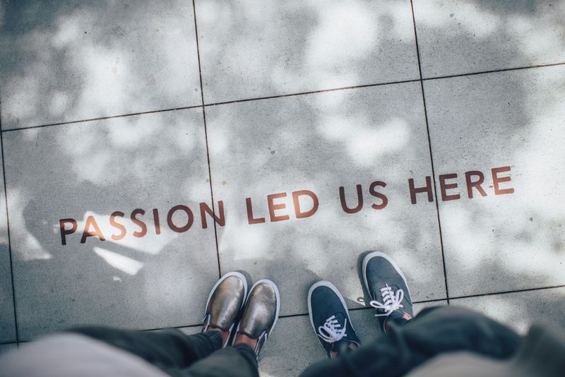 Two pairs of feet standing in front of a sidewalk emblem that reads 'Passion Led Us Here'.