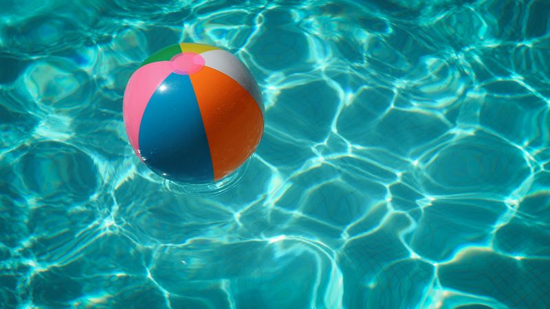 Photo of a colorful beach ball floating on the blue, reflective water of a swimming pool. 