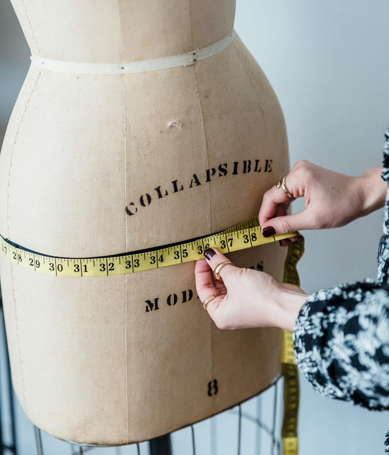 Someone wrapping a fabric tape measure around a sewing dummy.