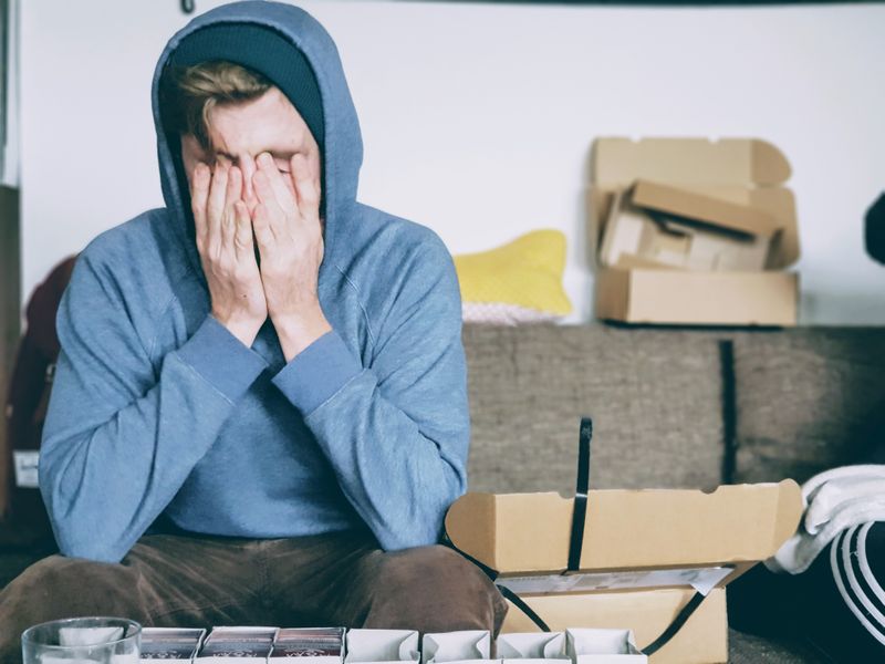 Man in blue hood covers his face with his hands looks overwhelmed 