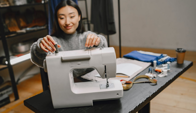 A woman installing a spool of thread on the top of a sewing machine.