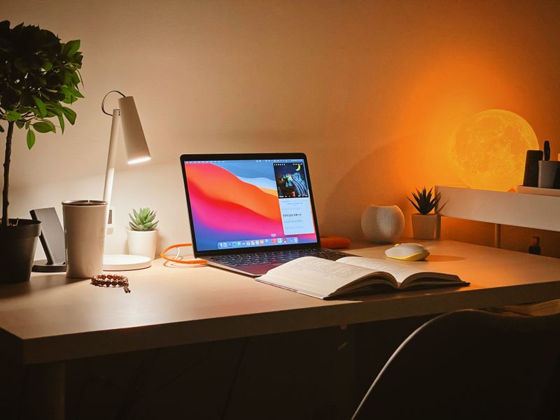 A neat desk with a laptop, course book, and a few lights and plants.