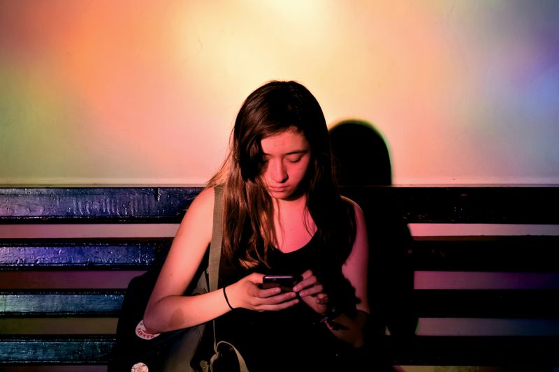 A girl sitting on a bench and looking at her phone.