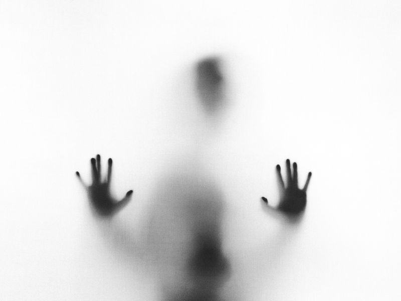 A blurred silhouette of a person with their hands pressed against glass.  