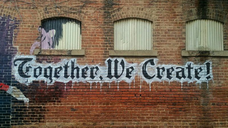 An old building with graffiti written in Gothic font that says 'Together, We Create!'