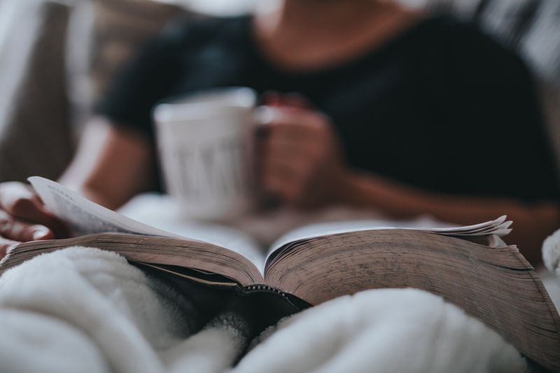 A person reading a book while sipping on a drink.