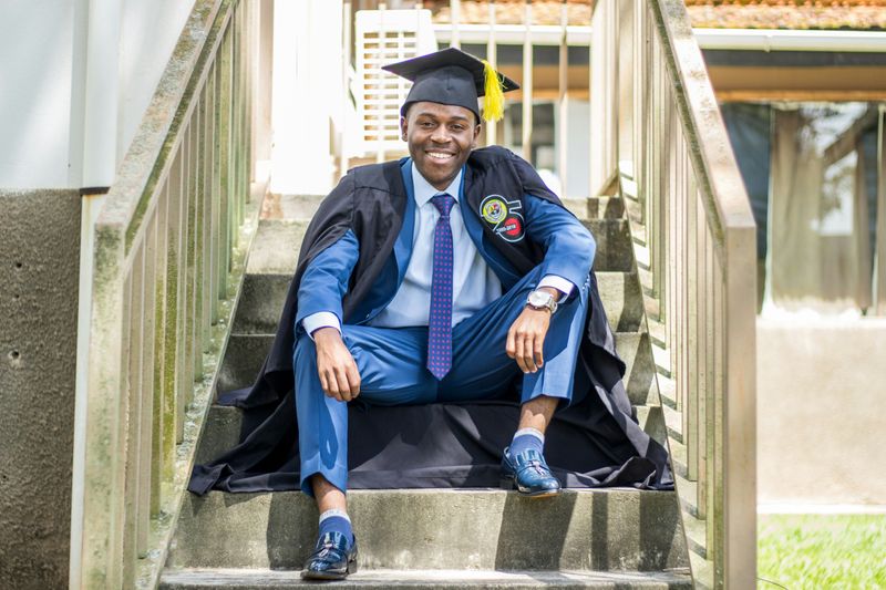 A Black male student in a graduation cap & gown.