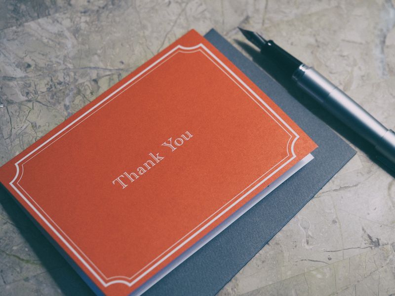 A red thank you card with white type on a marble countertop, with a silver fountain pen beside the card.