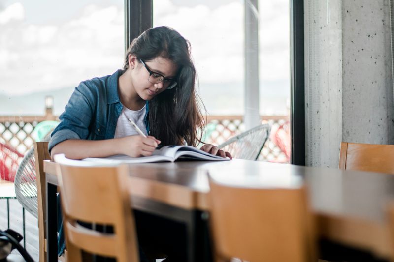 A young woman sitting at table writing in notebook.