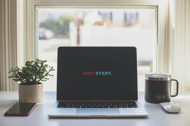 A minimalist workspace with a laptop displaying the motivational phrase “Just Start”.