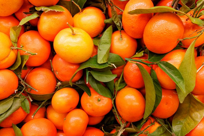 A pile of oranges with green leaves and stems attached.