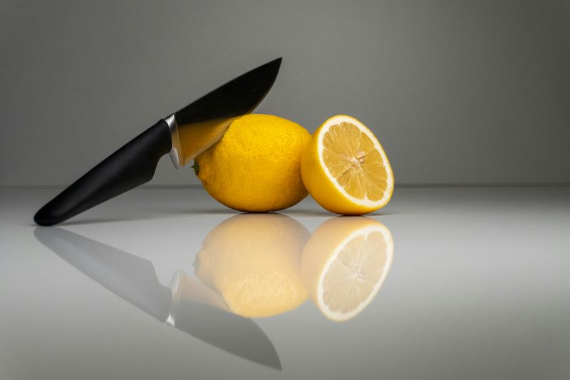 A knife slicing into a whole lemon, with another half lemon leaning on it. 