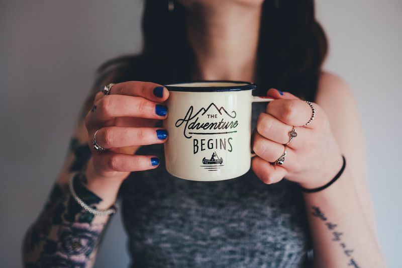 Close up of a tattooed woman holding a mug that reads 