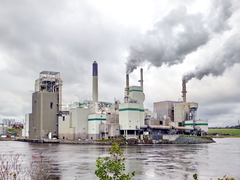 A factory on a river, with smoke coming out of stacks