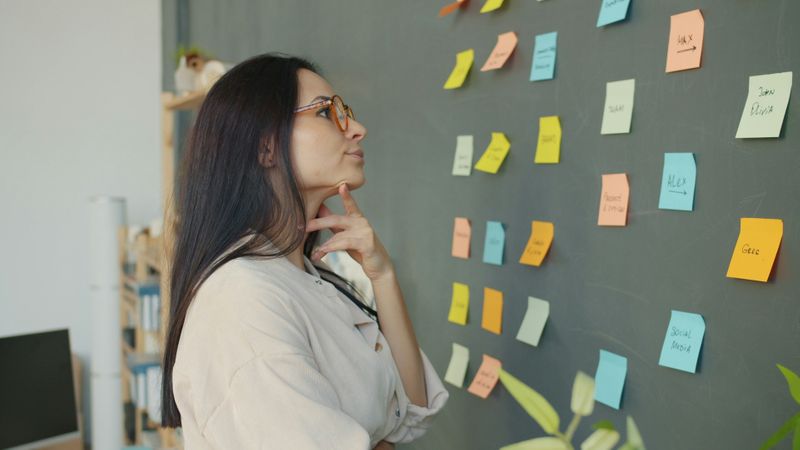 Woman looking at a chalkboard full of post it notes