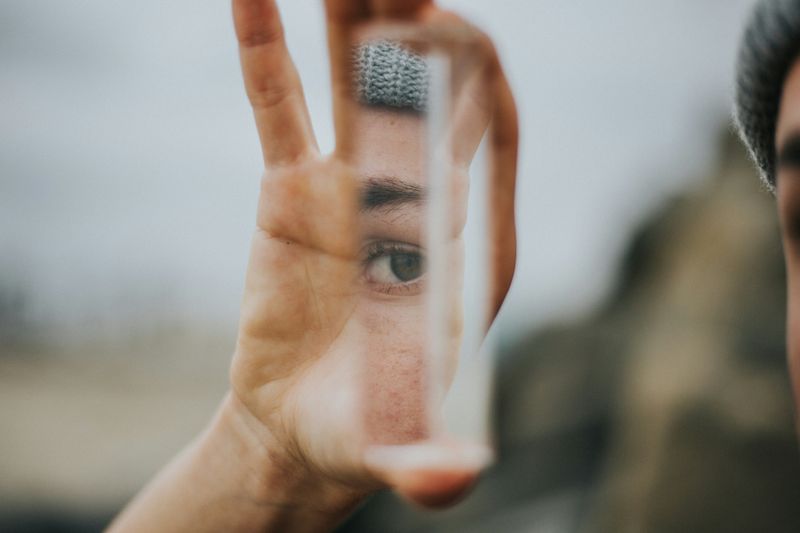 A prism held up by a woman, showing a partial reflection of her face and eye.