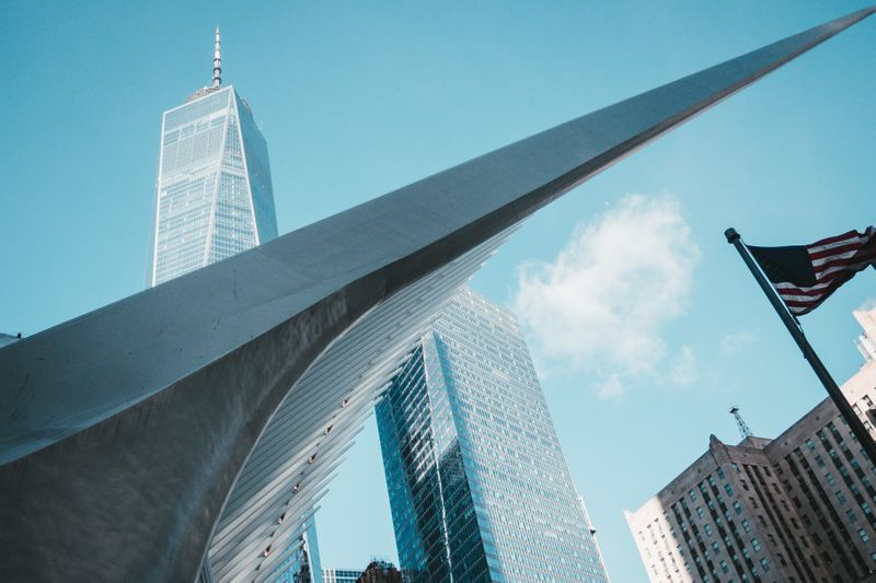 Photo of glass-windowed office, skyscraper buildings, against a backdrop of a light blue sky  